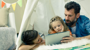 Szene im Kinderzimmer: Vater liest seinen Kindern eine Geschichte von einem Tablet-Computer vor.