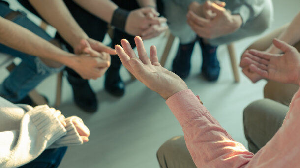 Nahaufnahme: die Hände mehrerer Personen, die im Kreis zusammensitzen. 