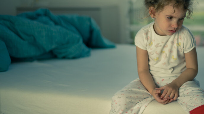 Ein Kind sitzt allein auf einem Bett.