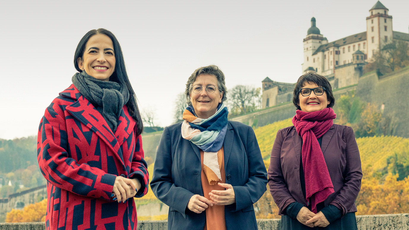 Drei Frauen schauen lachend in die Kamera. Im Hintergrund: eine Burg.